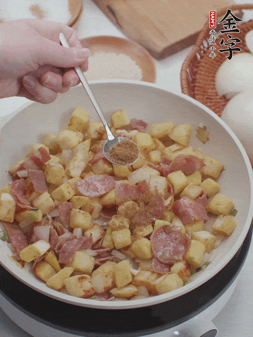 起鍋少油，煸香洋蔥丁、蔥白，加入金字培根火腿翻炒幾下，再加入饅頭丁、1小勺孜然粉、少許鹽翻炒均勻并鋪平。